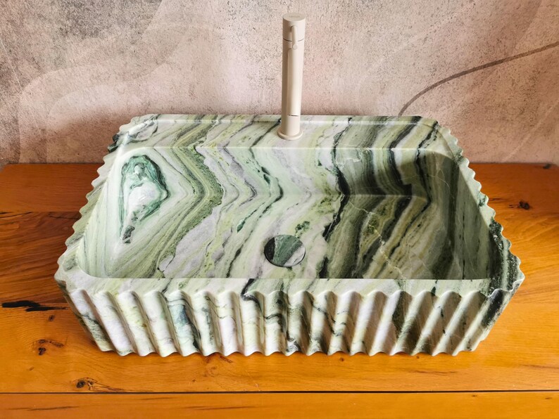 May include: A rectangular, green and white marble sink with a decorative, ridged edge. The sink has a circular drain and a tall, off-white faucet. The marble has a natural, flowing pattern.