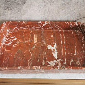 May include: A rectangular red and white marble sink with a smooth, polished surface.