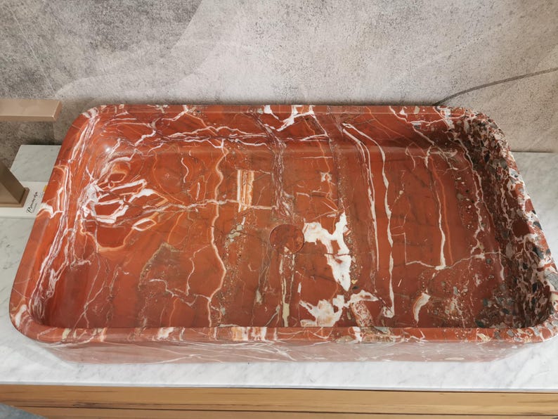 May include: A rectangular red and white marble sink with a smooth, polished surface.