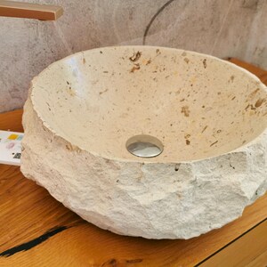 Lavabo in marmo beige visto frontalmente con forma rotonda, interno chiaro e superficie esterna rocciosa