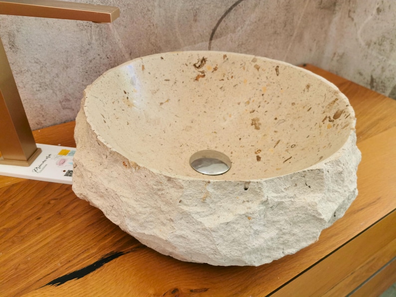 Lavabo in marmo beige visto frontalmente con forma rotonda, interno chiaro e superficie esterna rocciosa