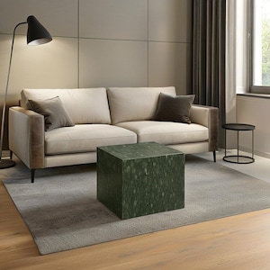 May include: A green marble cube coffee table with a white sofa and a black floor lamp in the background.