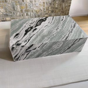 May include: A large, rectangular, green and black marble pedestal. The marble has a swirling pattern of black and white veins.