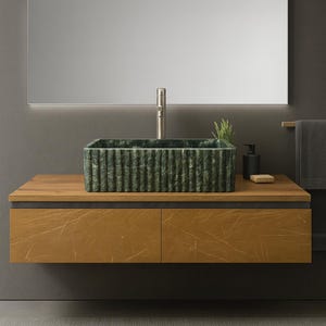 May include: A modern bathroom vanity with a rectangular green marble sink. The sink sits on a wooden cabinet with two drawers. A large mirror is above the sink, and a stainless steel faucet is installed. A soap dispenser and a small plant are on the counter.