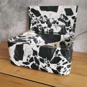 May include: A black and white marble sink with a backsplash. The sink has a rectangular shape with a curved front and a backsplash with three holes. The marble has a unique pattern of black and white veining.
