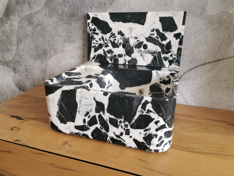 May include: A black and white marble sink with a backsplash. The sink has a rectangular shape with a curved front and a backsplash with three holes. The marble has a unique pattern of black and white veining.