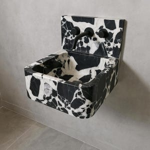 May include: A wall-mounted sink with a striking black and white marble pattern. The sink has a rectangular basin and a matching backsplash. It features a black faucet and two black knobs. The overall design is modern and minimalist.