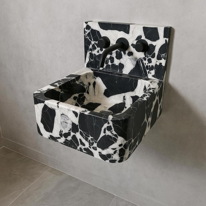 May include: A wall-mounted sink with a striking black and white marble pattern. The sink has a rectangular basin and a matching backsplash. It features a black faucet and two black knobs. The overall design is modern and minimalist.