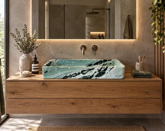 Può includere: Un lavabo rettangolare in marmo venato verde e nero, montato su un mobile da bagno sospeso in legno di rovere chiaro con due cassetti. Il lavabo presenta una finitura lucida con motivi e texture in pietra naturale molto evidenti.