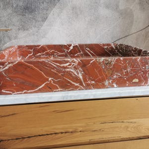 May include: A rectangular red marble sink with white veining. The sink is sitting on a wooden countertop.