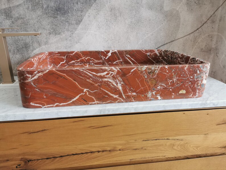May include: A rectangular red marble sink with white veining. The sink is sitting on a wooden countertop.