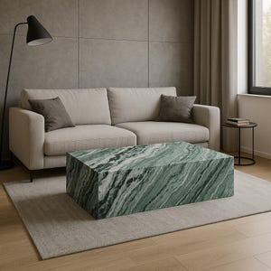 Op de afbeelding: Een groene marmeren salontafel met een wit en groen swirl-patroon. De tafel staat op een lichtgrijs tapijt voor een beige bank.