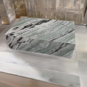 May include: A large, rectangular, green and black marble coffee table with a swirling pattern. The table is sitting on a light grey tiled floor.