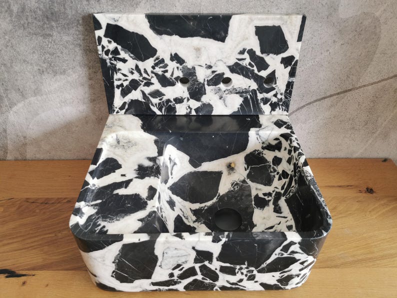 May include: A black and white marble-patterned soap dish with a hinged lid. The dish has a rectangular base with rounded corners and a divided interior. The lid features a similar pattern and has several small holes.