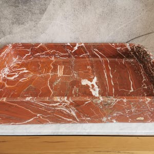 May include: A rectangular red and white marble sink with a smooth, polished surface.