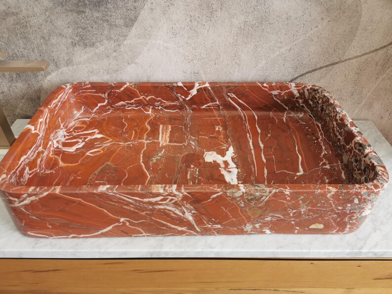 May include: A rectangular red and white marble sink with a smooth, polished surface.