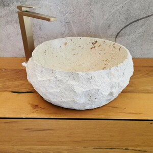 Vista frontale del lavabo da bagno in pietra naturale beige con esterno grezzo e bordo irregolare