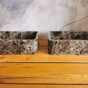 May include: Two rectangular bathroom sinks crafted from dark brown and grey marble with prominent white veining. Each basin features a smooth, polished finish and a deep, open interior, showcasing the natural stone patterns and textures.