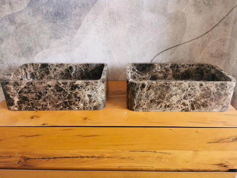 May include: Two rectangular bathroom sinks crafted from dark brown and grey marble with prominent white veining. Each basin features a smooth, polished finish and a deep, open interior, showcasing the natural stone patterns and textures.