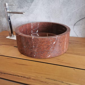 Op de afbeelding: Een ronde wastafel van rood marmer met witte aderen. De wastafel staat op een houten aanrechtblad.