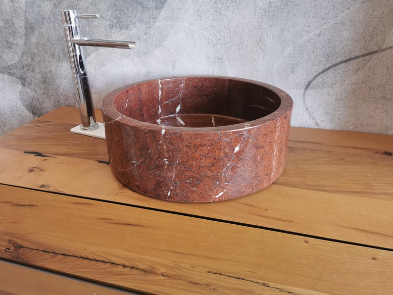 Op de afbeelding: Een ronde wastafel van rood marmer met witte aderen. De wastafel staat op een houten aanrechtblad.