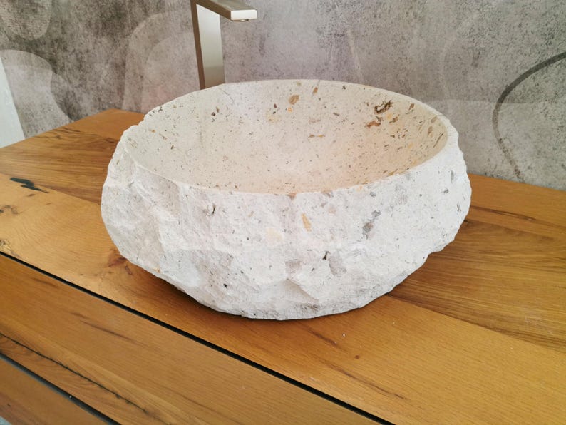 Lavabo rotondo in marmo beige visto lateralmente con lavorazione esterna grezza e tonalità crema