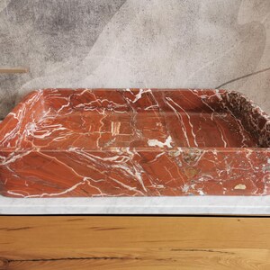 May include: A rectangular red marble sink with white veining. The sink is sitting on a wooden countertop.