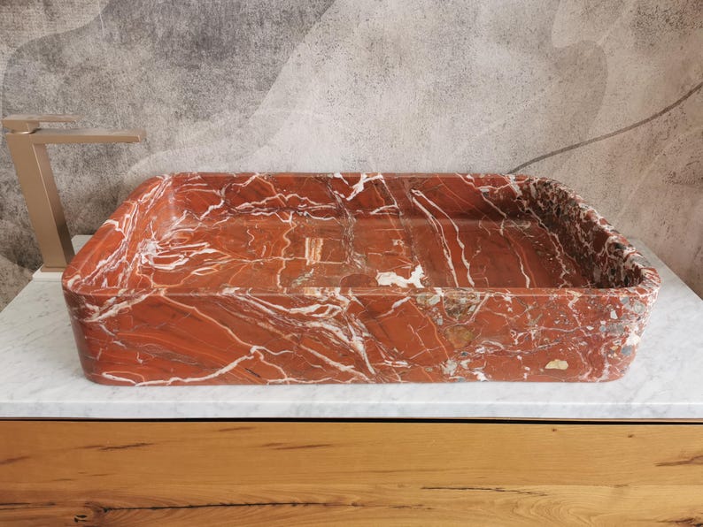 May include: A rectangular red marble sink with white veining. The sink is sitting on a wooden countertop.