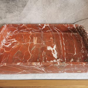 May include: A rectangular red and white marble sink with a smooth, polished surface.