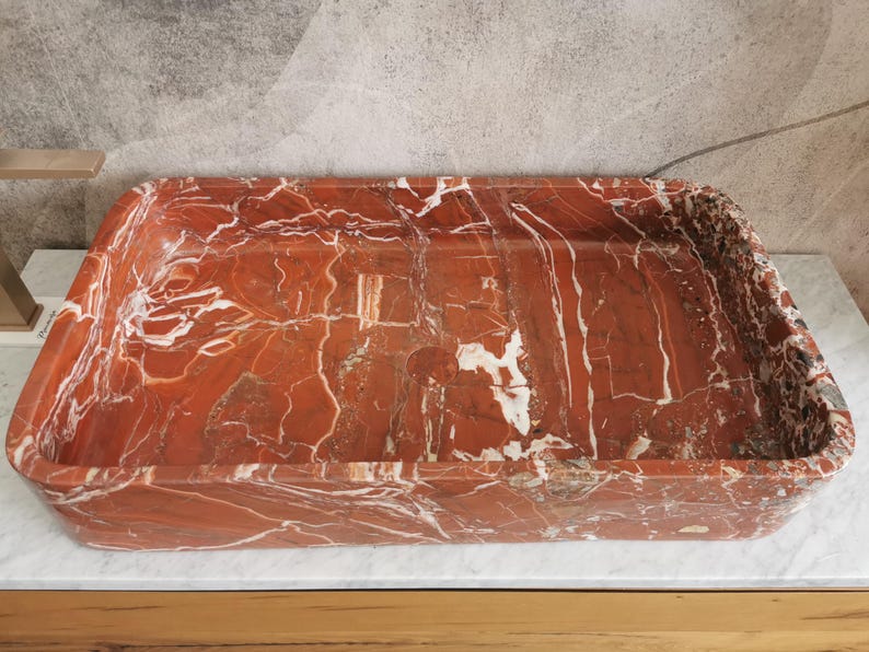 May include: A rectangular red and white marble sink with a smooth, polished surface.