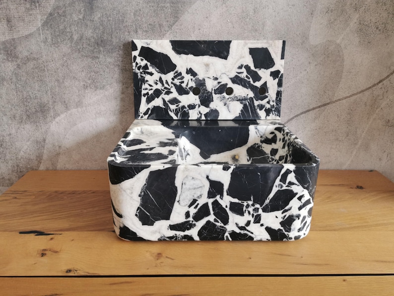 May include: A black and white marble-patterned box with a hinged lid. The box has a rectangular shape with rounded corners and a smooth, polished finish. The lid is open, revealing the interior of the box. The box is sitting on a wooden surface.