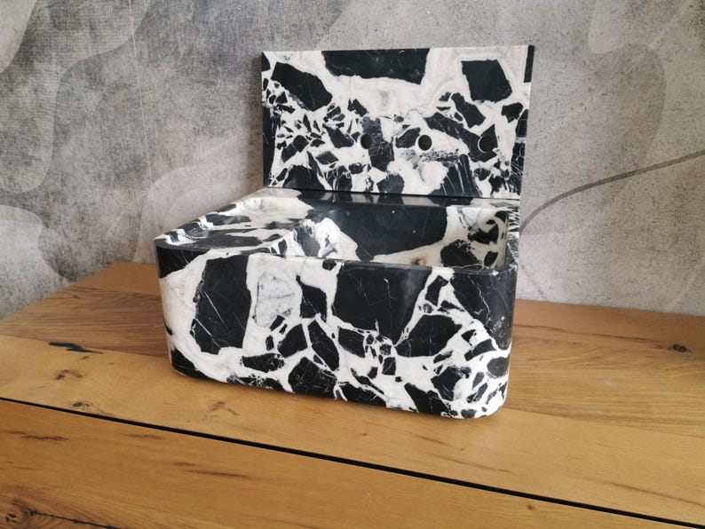 May include: A rectangular box with a hinged lid, crafted from a black and white terrazzo-style material. The box is open, revealing its interior. The design features a striking contrast of black and white, creating a modern aesthetic.