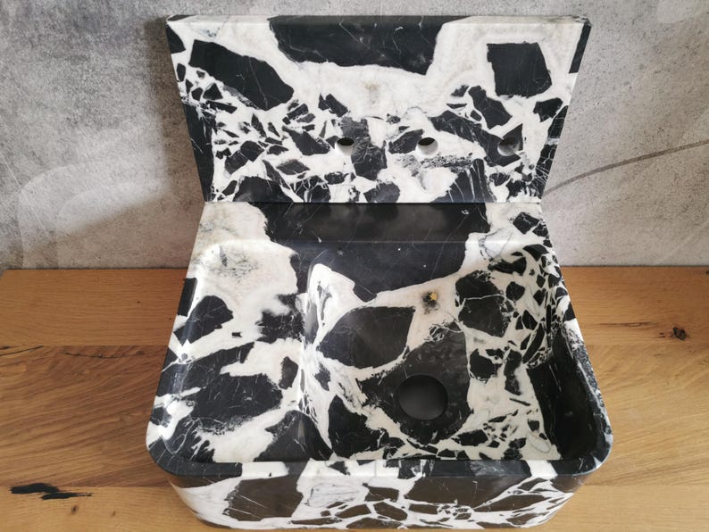 May include: A black and white marble sink with a unique, angular design. The sink features a rectangular basin with a curved front and a raised, angled back. The marble has a striking pattern of black and white veining.