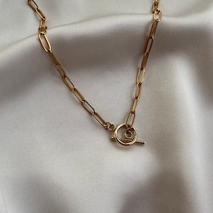 Könnte beinhalten: Eine goldene Kettenkette mit einem Toggle-Verschluss. Die Kette besteht aus miteinander verbundenen ovalen Formen.