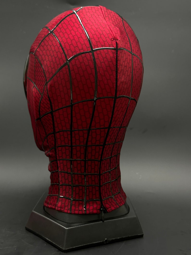 May include: Red and black Spider-Man mask with a detailed web design. The mask is on a black stand.