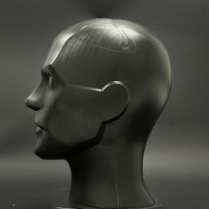 May include: A black mannequin head with a smooth, matte finish. The head is tilted slightly to the side, and the eyes are closed. The head is mounted on a black base.