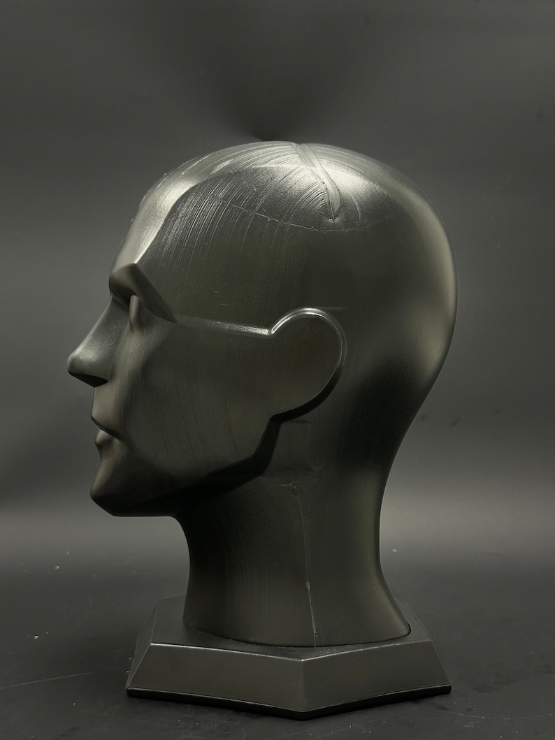 May include: A black mannequin head with a smooth, matte finish. The head is tilted slightly to the side, and the eyes are closed. The head is mounted on a black base.