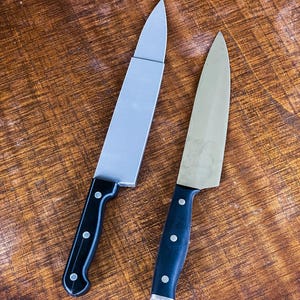 May include: Two kitchen knives with silver blades and black handles. One knife has a rectangular blade, the other has a curved blade. Both knives have three rivets on the handle. The knives are on a wooden surface.