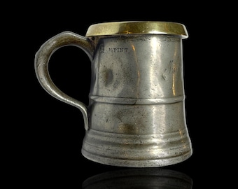 Jarra antigua de peltre de media pinta con borde de latón. Grabada y estampada.