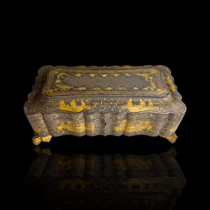 May include: An antique, rectangular box with a hinged lid. The box is primarily dark with gold accents, featuring ornate designs and a scalloped edge. The box sits on small, decorative feet and is reflected in the glossy surface below.