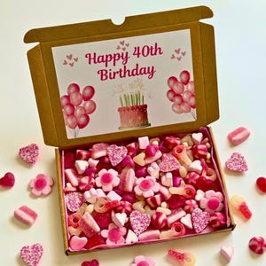 May include: A brown cardboard gift box filled with pink and red candies, including hearts, flowers, and gummy shapes. The box lid features a printed design with the text "Happy 40th Birthday", balloons, and a cake.