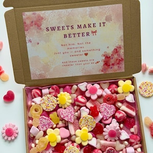 Könnte beinhalten: Eine Pappschachtel gefüllt mit einer Vielzahl bunter Süßigkeiten, darunter Blumen-, Herz- und Ringformen. Der Deckel der Schachtel trägt den Text "SWEETS MAKE IT BETTER". Die Süßigkeiten sind in Rosa-, Gelb- und Rottönen gehalten.