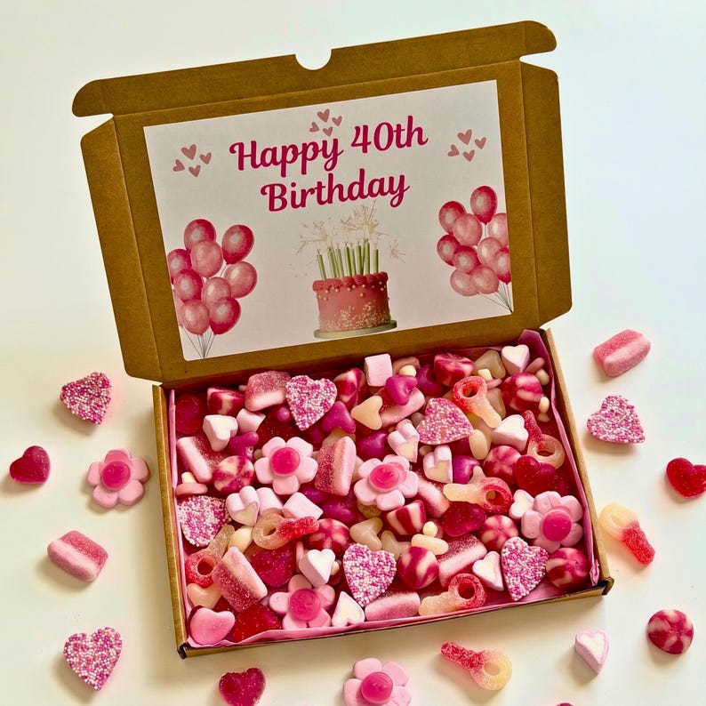 May include: A brown cardboard gift box filled with pink and red candies, including hearts, flowers, and gummy shapes. The box lid features a printed design with the text "Happy 40th Birthday", balloons, and a cake.