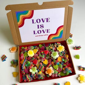 May include: A brown cardboard box with a lid displaying a rainbow design and the words "LOVE IS LOVE and always will be." The box is filled with colourful gummy sweets in flower, heart, and rainbow shapes. Some sweets are scattered around the box.