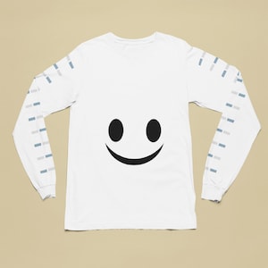 Op de afbeelding: Witte longsleeve t-shirt met een zwarte smiley-gezichtsgrafiek op de voorkant en een grijs-wit gestreept patroon op de mouwen.
