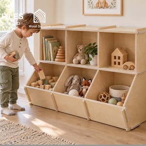 Può includere: Un mobiletto portagiochi in legno chiaro dotato di tre ripiani rettangolari superiori e tre contenitori inclinati inferiori. L'unità è riempita con vari giocattoli, tra cui libri, un orsacchiotto, una casetta in legno e blocchi da costruzione.