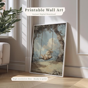 May include: A framed print featuring a whimsical illustration of a bunny on a swing. The artwork is set against a backdrop of trees and a cloudy sky, with the text "Printable Wall Art" and "Instant Digital Download". The print is ready to hang.