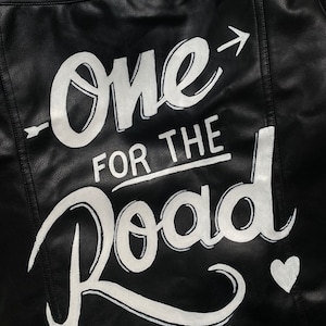 Może przedstawiać: Czarna skórzana kurtka z białym napisem "one for the road" ze strzałką skierowaną w prawo i małym białym sercem.