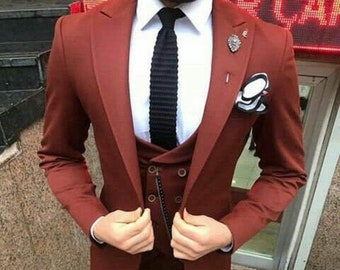 May include: A three-piece suit in a deep reddish-brown color. The suit includes a blazer, vest, and trousers. A white dress shirt and black tie are worn underneath. A pocket square and lapel pin add detail. Black leather shoes complete the ensemble.