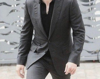 May include: A charcoal gray suit, featuring a tailored jacket with a two-button closure and matching trousers. The suit is paired with a black collared shirt. The person is walking up a set of stairs.
